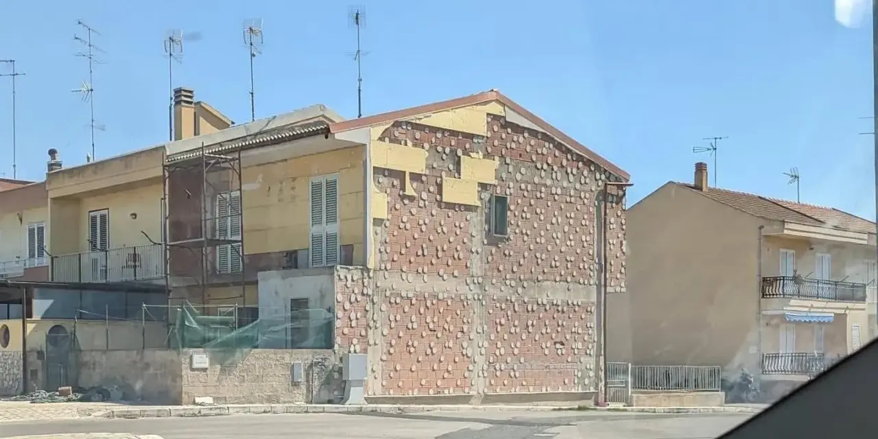 Edificio in fase di ristrutturazione, con facciata parzialmente scoperta che rivela la muratura. Sembra un condominio in attesa del suo nuovo cappotto.