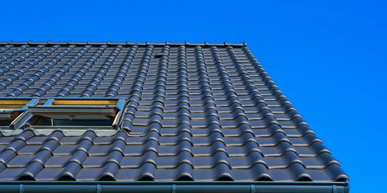 Coperture tetti moderni in tegole scure, con lucernari a vista sotto un cielo azzurro intenso.