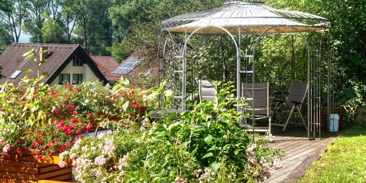 Un gazebo con un pavimento in legno fai da te, circondato da fiori colorati e vegetazione lussureggiante.