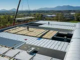 Operai installano pannelli isolanti su un tetto, riducendo il rumore. Un cantiere in corso con montagne sullo sfondo.