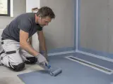 Operaio applica uno strato di impermeabilizzazioni edili con un rullo, preparando una doccia a filo pavimento.