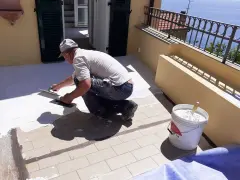 Operaio applica uno strato bianco per come impermeabilizzare un terrazzo. Secchio di materiale pronto all'uso.