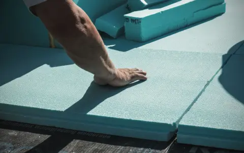 Mano che posiziona pannelli isolanti azzurri, materiali per cappotto termico, su membrana impermeabile.