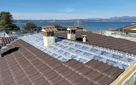Tegole tetto moderne marroni in fase di posa su un tetto con vista lago. Sotto le tegole, una membrana isolante.
