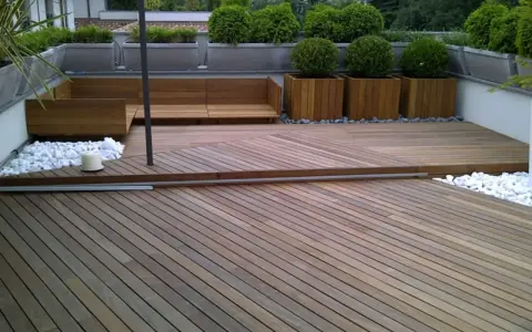 Un balcone trasformato con un pavimento in legno fai da te, circondato da piante e arredi moderni.