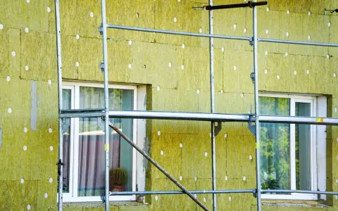 Installazione di un cappotto termico su un edificio, con ponteggi metallici che circondano la facciata isolata. La durata del cappotto termico è garantita da materiali di qualità.