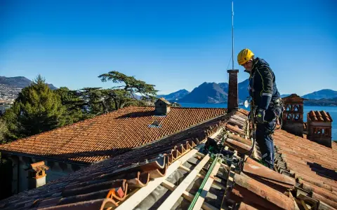 Operaio con imbracatura lavora alla costruzione tetti in legno, con vista su lago e montagne.