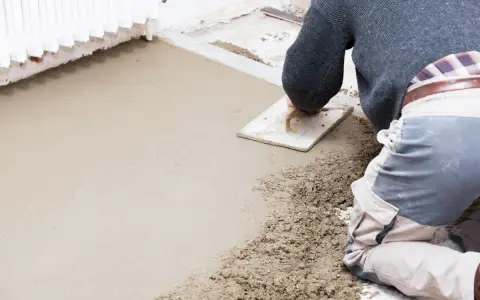 Operaio al lavoro con una cazzuola, livella il cemento per aumentare l'altezza del pavimento.