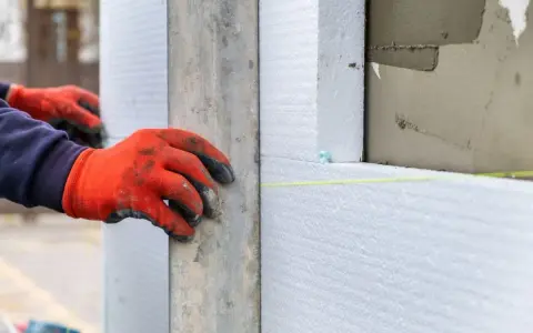Mani con guanti rossi posano pannelli di polistirene estruso, materiale isolante per l'edilizia.
