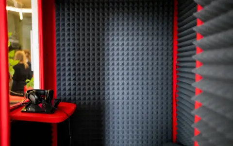 Cabina insonorizzata con pannelli fonoassorbenti, cuffie e tablet. Ideale per registrazioni audio.