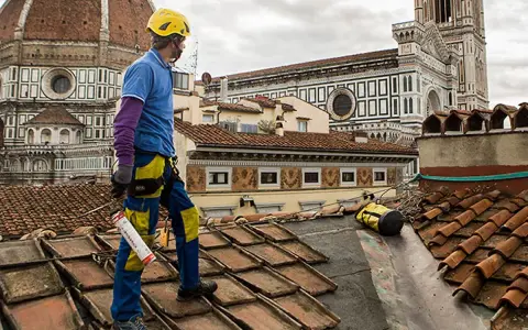 Operaio sul tetto di Firenze, valuta il costo coibentazione tetto esistente. Lavori in quota con vista Duomo.