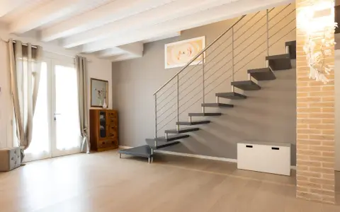 Moderna scala a sbalzo, soluzione per chi ha una scala troppo ripida. Arredamento minimalista con mobili in legno e tessuti chiari.