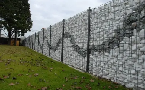 Muro di recinzione moderno con gabioni riempiti di pietre bianche e grigie, creando un motivo ondulato. Ottime idee muri di recinzione per un giardino.