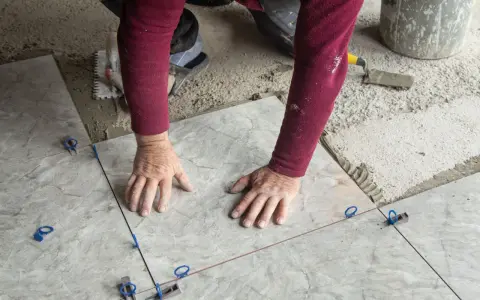 Mani esperte posano mattonelle con precisione, usando livellatori per un risultato perfetto.