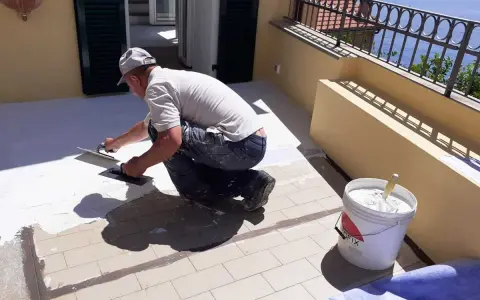 Operaio applica uno strato bianco per come impermeabilizzare un terrazzo. Secchio di materiale pronto all'uso.