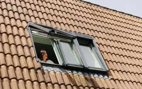 Donna guarda fuori da una finestra sul tetto, un esempio di come isolare il tetto dall'esterno per un maggiore comfort.