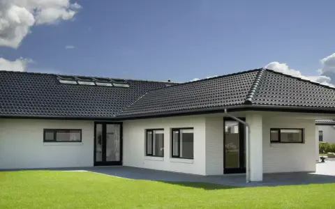 Casa moderna con tetto a padiglione scuro, finestre a tetto e prato verde.