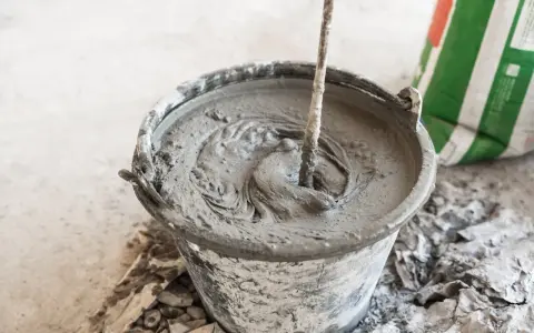 Secchio con malta fresca in preparazione, mostrando la differenza tra malta e cemento. Un sacco di cemento è visibile sullo sfondo.