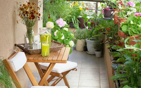 Un terrazzo fiorito e accogliente, perfetto per chi cerca idee su come abbellire un terrazzo fai da te. Tavolino in legno con bevanda rinfrescante e fiori colorati.