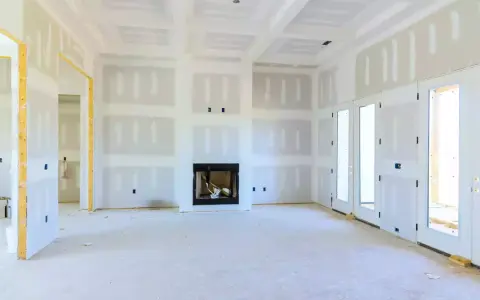 Interno di una casa in costruzione con pareti e soffitto in cartongesso, camino e porte a doppio battente.
