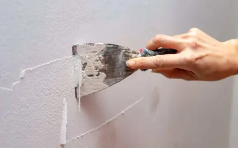 Mano usa una spatola per rimuovere la vecchia pittura, mostrando come grattare un muro per prepararlo.