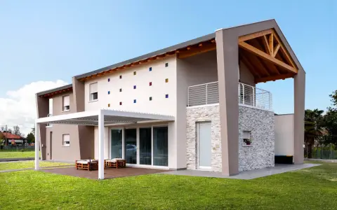 Casa moderna con tetto in legno a vista, facciata decorata con quadrati colorati e un portico bianco.