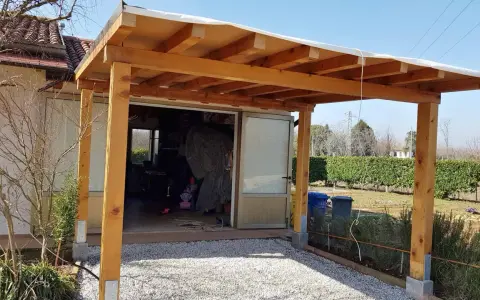Una tettoia fai da te in legno protegge un'entrata, con un tetto in telo bianco e pilastri robusti.
