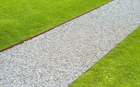 Un percorso di ghiaia bianca delimita un prato verde brillante, creando un vialetto giardino invitante.