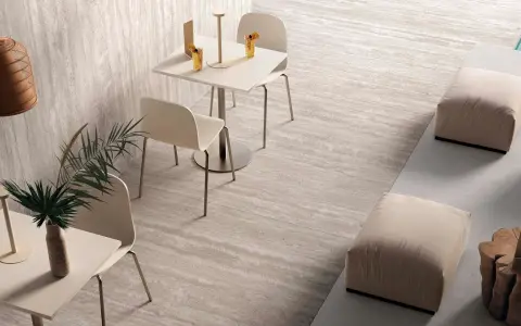 Un caffè moderno con tavolini, sedie e pouf, su eleganti pavimenti senza fughe effetto pietra.
