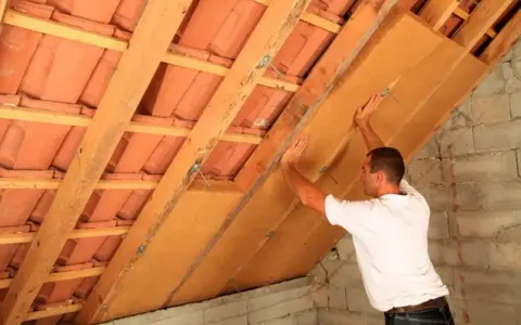 Operaio installa pannelli per la coibentazione del tetto in legno, migliorando l'isolamento termico.