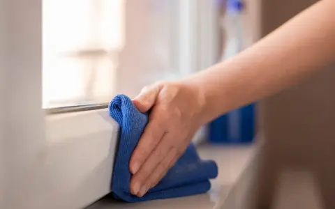 Mano pulisce davanzale in PVC effetto legno con panno blu. Scopri come pulire pvc effetto legno per mantenerlo come nuovo.