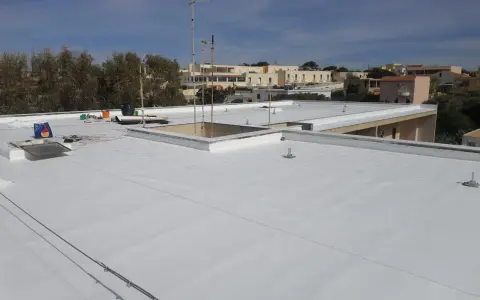 Tetto piano bianco appena impermeabilizzato senza rifarlo, con antenne e edifici sullo sfondo.