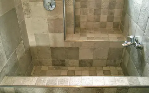 Bagno con vasca da bagno in muratura fai da te, rivestita con piastrelle grigie di varie tonalità e fantasie.