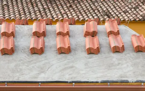 Pezzi di tutti i tipi di tegole rosse impilati su un tetto in cemento, pronti per essere posati.