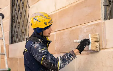 Operaio con casco giallo applica soluzione per pulire muro esterno con candeggina.