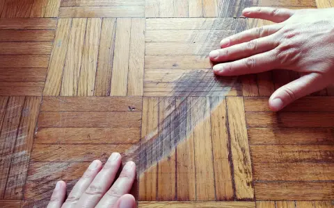 Mani sul parquet rovinato, mostrando i graffi e le macchie. Si valuta come pulire il parquet rovinato per riportarlo al suo antico splendore.