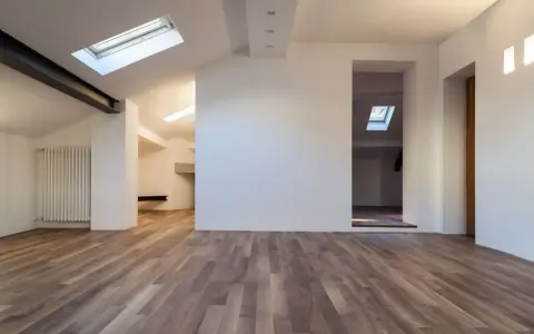 Interno moderno con pavimenti in legno e pareti in cartongesso sottotetto. Finestre sul tetto illuminano lo spazio.