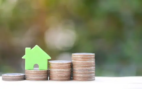 Una casa verde su pile di monete, un'immagine che simboleggia come funziona il Superbonus 110 per l'edilizia.