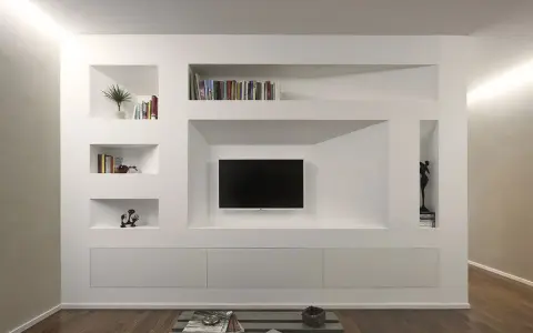 Parete attrezzata moderna con nicchie per libri e TV, realizzata in cartongesso doppia lastra, con mobili contenitori a scomparsa.