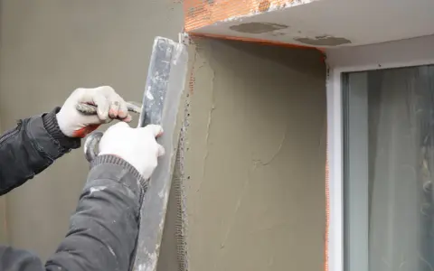Lavori di intonacatura attorno alle finestre, con un cappotto che protegge le spallette. Si nota lo spessore dello strato di intonaco.