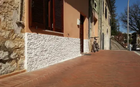 Una parete umida è stata rivestita con pietre bianche, migliorando l'estetica e la protezione dell'edificio.