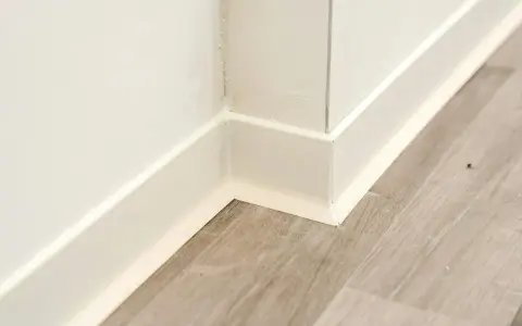 Angolo di una stanza con pavimento in laminato grigio e battiscopa bianco appena posato.
