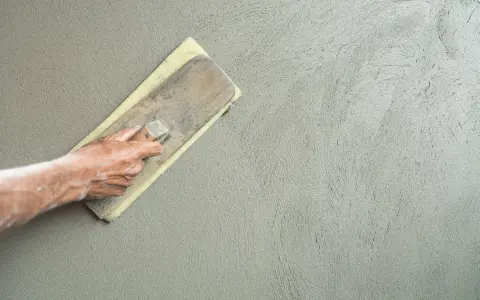 Mano che stende l'intonaco con una spatola. Dopo l'intonaco posso pitturare la parete.