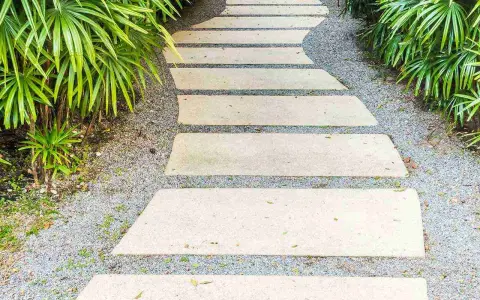 Un sentiero sinuoso con lastre di pietra e ghiaia, circondato da vegetazione lussureggiante. Idee marciapiede casa per un ingresso accogliente.