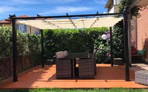 Un patio con tavolo e sedie sotto una pergola, con un **pavimento esterno economico fai da te** color terracotta.