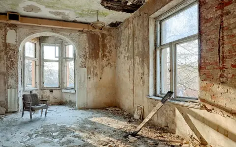 Interno di una casa a botte in rovina, con pareti scrostate, soffitto sfondato e un vecchio mobile.