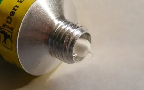 Tubo di alluminio con crema bianca che fuoriesce, mostrando diversi tipi di silicone.