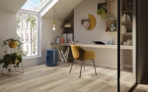 Luminoso studio mansardato con scrivania, sedia gialla e un elegante **pavimento polvere di pietra** che riflette la luce naturale.