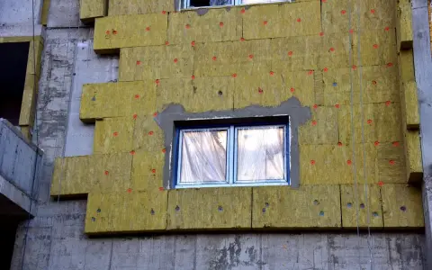 Pannelli di lana di roccia per cappotto termico spessore, fissati con tasselli rossi su un edificio in costruzione.