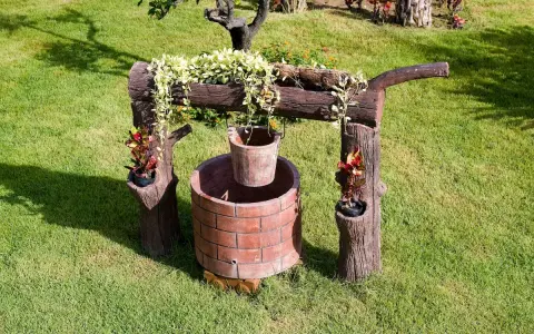 Pozzo decorativo in mattoni con secchio appeso, circondato da verde. Un'idea per capire quanto costa fare un pozzo.